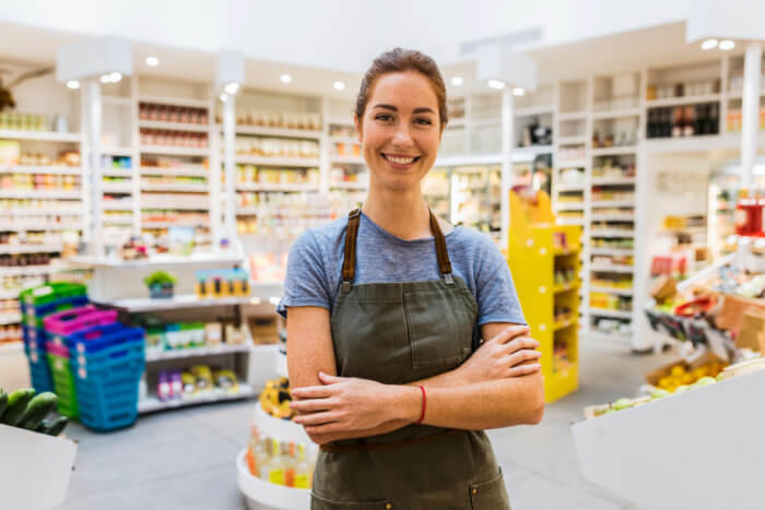 Happy,Natural,Young,Saleswoman,In,Modern,Supermarket.,Cross,Arms.,Looking