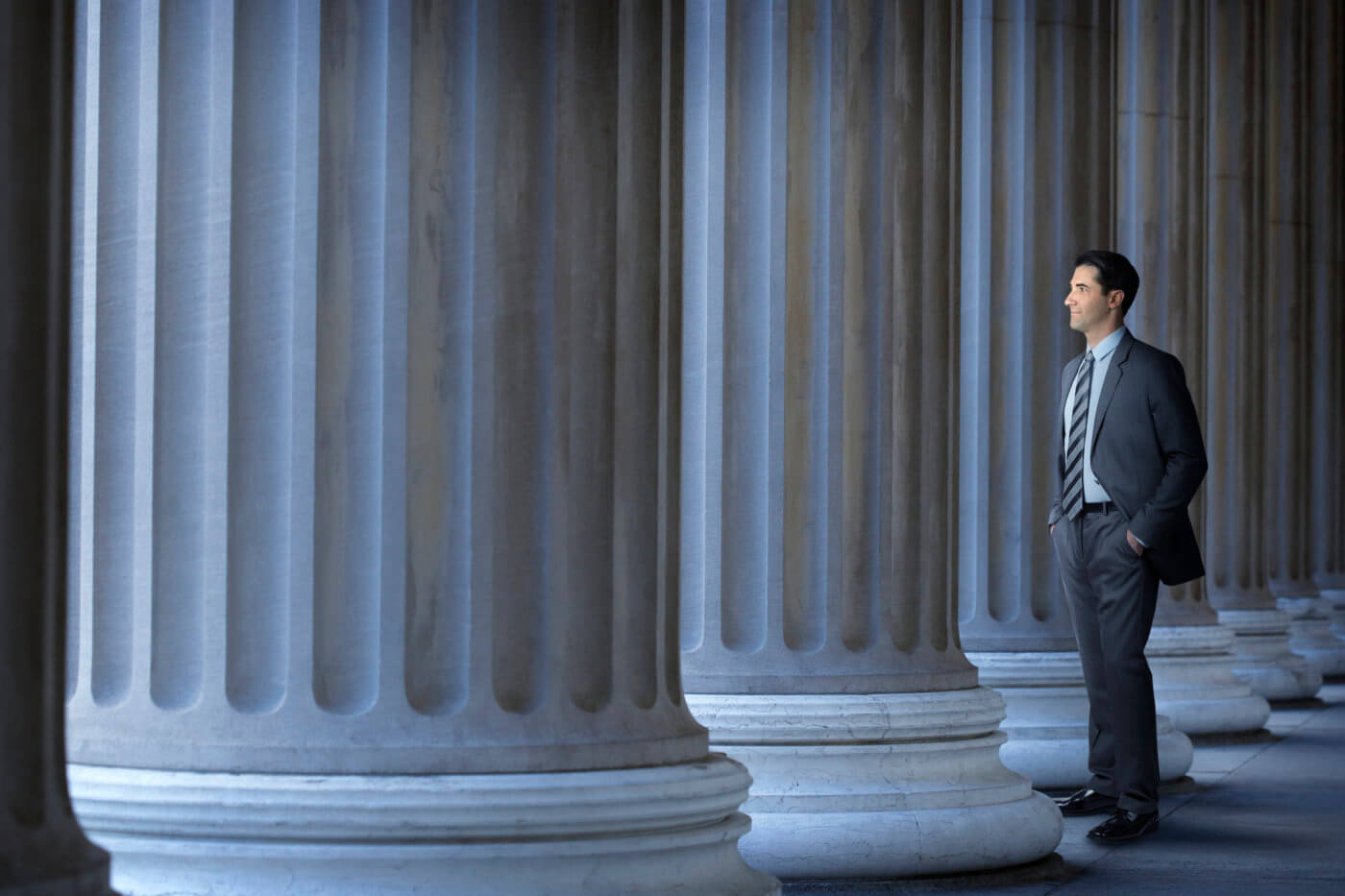 A lawyer, banker, or businessman standing among large columns looking out into the distance.